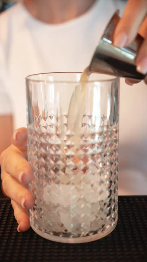 Bartender pours a cloudy yellow citrus mixture into a textured glass filled Stock Footage 346719040