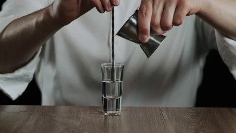 The bartender pours irish cream from jigger to cocktail glass with sambuca Stock Footage 133960141