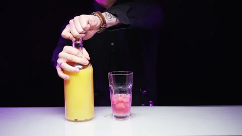 Bartender pours orange juice from bottle into a glass glass glass with pink ice Stock Footage 168967729