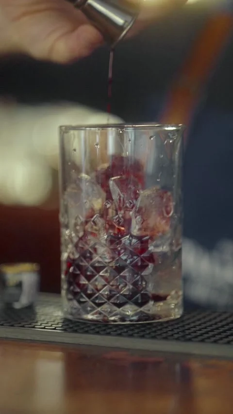 A bartender pours a shot of alcohol from a jigger into a glass with crushed ice. Stock Footage 271661985