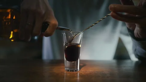 Bartender pours transparent alcohol to the layered shot with dark liquor Stock Footage 143589095