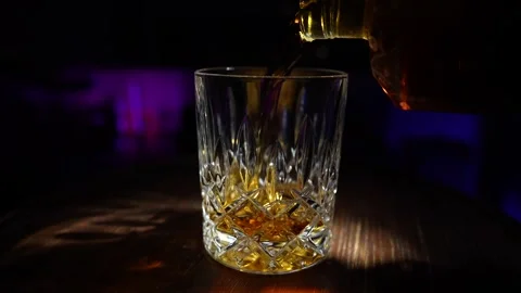 Bartender pours whiskey from bottle into crystal glass, close up, slow motion Stock Footage 296609082