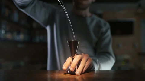 Bartender pours whiskey to the jigger and then to the glass with ice Stock Footage 143589013