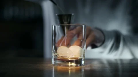 Bartender pours whiskey to the jigger and then to the glass with ice Stock Footage 143589150