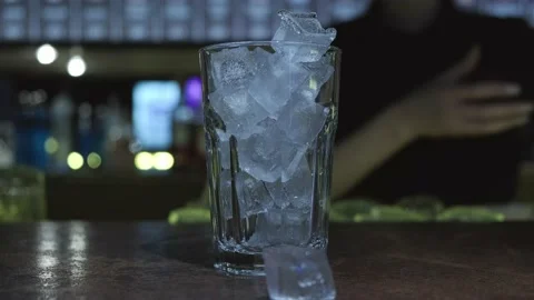 The bartender prepares a cocktail. She puts ice in a glass, pours the Stock Footage 157418886