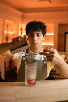 The bartender preparing a cocktail pours from a shaker into a glass using a s Stock Photos