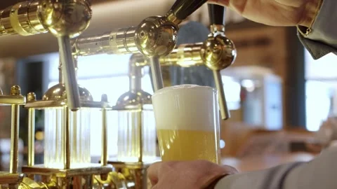Bartender pulls a glass of creamy lager beer from brass taps, low angle Stock Footage 272427494