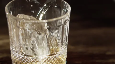 Bartender puts a piece of ice in a glass and pours the liquor, slow motion. Stock Footage 136545870