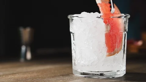 Bartender puts slice of grapefruit into glass with ice, slow motion. Stock Footage 123964150