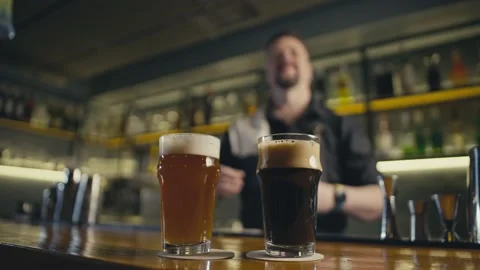 A bartender puts two glasses of beer on the bar in a pub. Video stock 234178189
