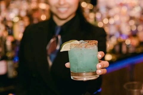 Bartender serving blue cocktail with lime garnish at a vibrant bar during Stock Photos