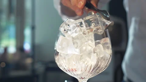 A bartender in a shirt takes an ice cube with tongs and puts it into glass Stock Footage 312553073