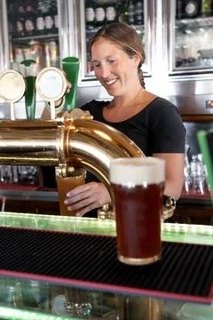 Bartender smiling while handing a glass of draft beer to a customer Stock Photos