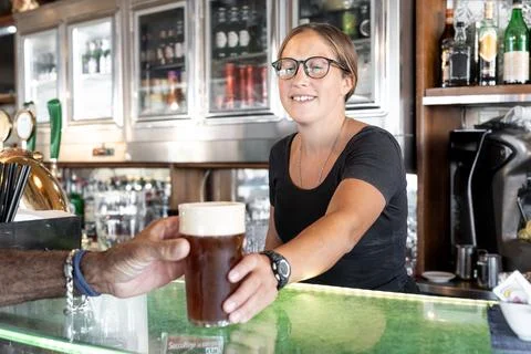 Bartender smiling while handing a glass of draft beer to a customer Stock Photos