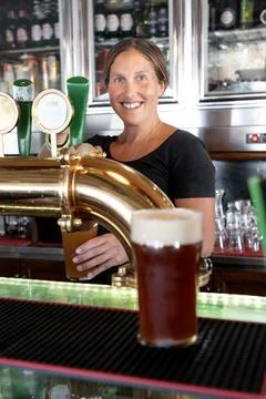 Bartender smiling while handing a glass of draft beer to a customer Stock Photos