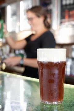 Bartender smiling while handing a glass of draft beer to a customer Stock Photos