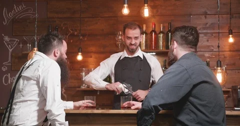 Bartender socializing with two bearded costumers and cleaning a glass Stock Footage 103933989