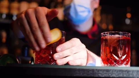 Bartender is squeezing out piece of orange peel and decorating cocktail. 库存影片 149126293