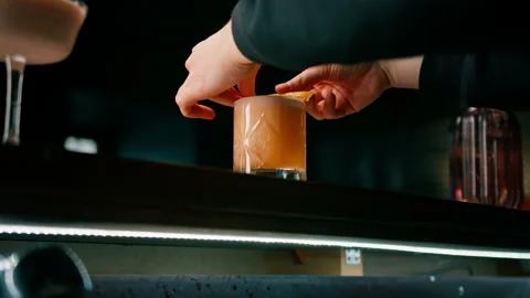 Bartender squeezing a piece of orange peel and garnishing a negroni cocktail at Stock Footage 240449552