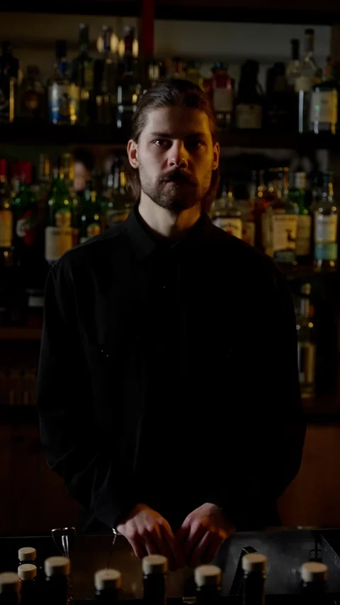 The bartender is standing behind the bar and looking at the camera against the Stock Footage 262636283