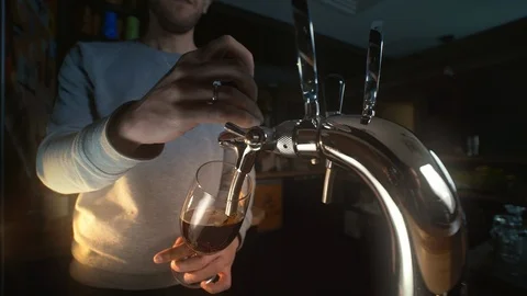 Bartender uses beer tap and pours draft beer to the glass in slowmotion, foamy Stock Footage 106359311