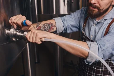 Bartender uses pipe to remove what is left in the big barrel. Stock Photos