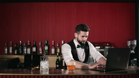 Bartender using laptop while standing behind bar counter 스톡 동영상 196857480