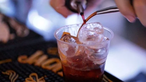 Bartender while he  is pouring the cocktail into the plastic cup at a bar Stock Footage 98237166