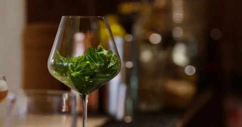Bartender's hand expertly crafts a mint-infused cocktail, blending fresh mint Stock Footage 304239219