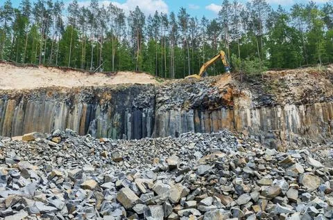Basalt mining. Excavators in a basalt quarry near the forest. Stock Photos