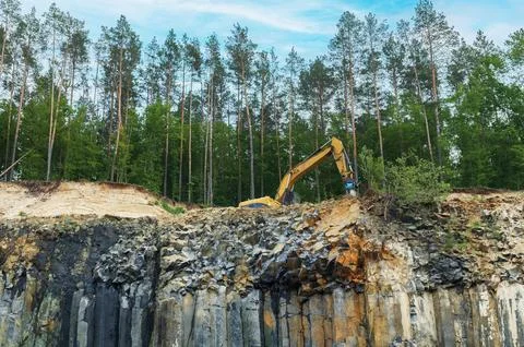 Basalt mining. Yellow excavators in a basalt quarry near the forest. Stock Photos