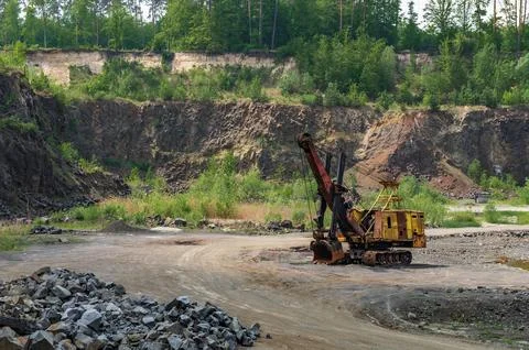 Basalt mining. Yellow excavators in a basalt quarry near the forest. Stock Photos