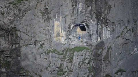 Base jumper soaring while descending near rock cliffs in Berner Oberland alps Stock Footage 79808682