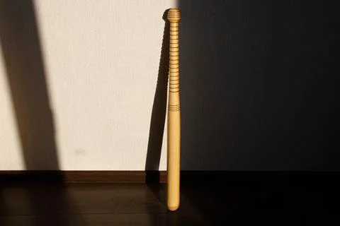 A baseball bat stands against the wall. Beautiful shadow of the sun Stock Photos
