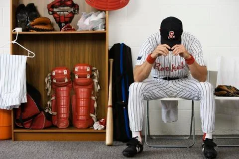 Baseball player sitting with head down in locker room Foto stock