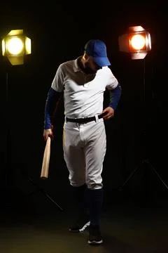 Baseball player in uniform holding bat adjusting belt under studio lights on  Stock Photos