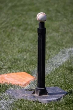 Baseball rests atop a black tee on grass Stock Photos