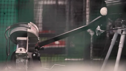 Baseball rolling down pitching machine ramp of indoor batting cage in slow Stock Footage 132138818