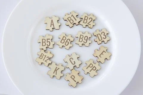 Basic essential vitamins for humans written on wooden puzzles on a white plate Stock Photos