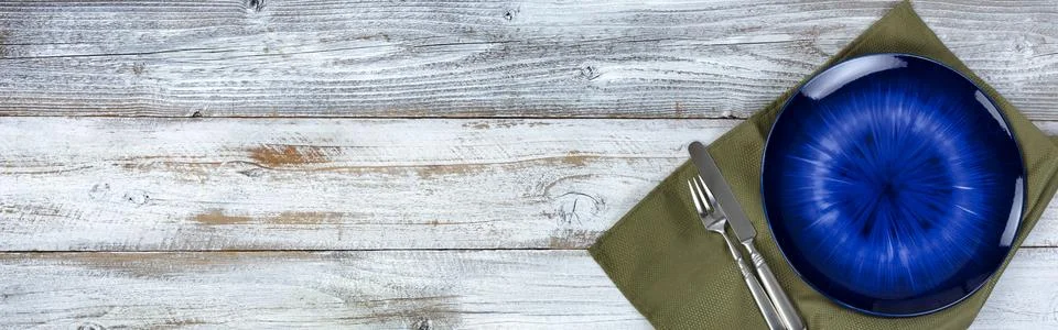 Basic table setting of an empty main dark blue dish with green cloth napkin.. Stock Photos