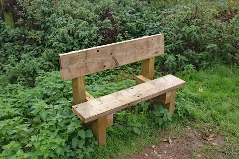 A basic timber bench set beside the canal towpath, for weary walkers to take  Stock Photos
