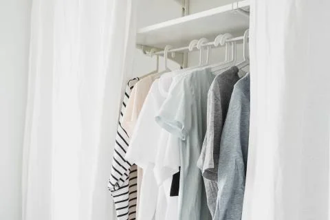 Basic women's clothes on a hanger, open wardrobe with textile curtains close- Stock Photos