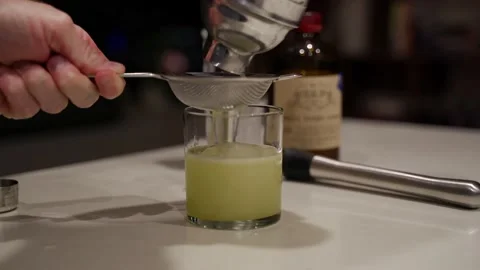 Basil gimlet filtered through metal strainer over a rocks cocktail glass Stock Footage 221592013