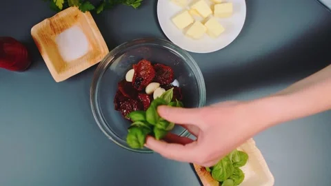Basil leaves fall into a plate with garlic and sun-dried tomatoes Video stock 249352045