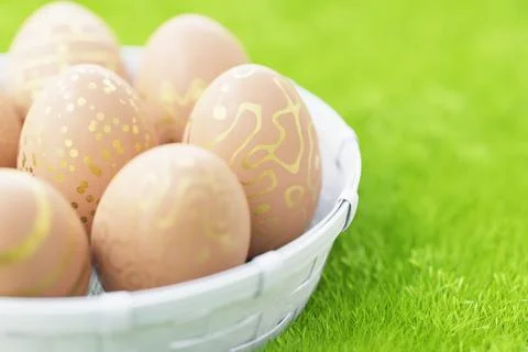 A basket of brown Easter eggs with a golden pattern in a basket on green gras Stock Illustration