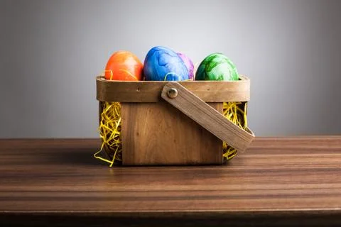 Basket, colored easter eggs on table, gray background Stock Photos