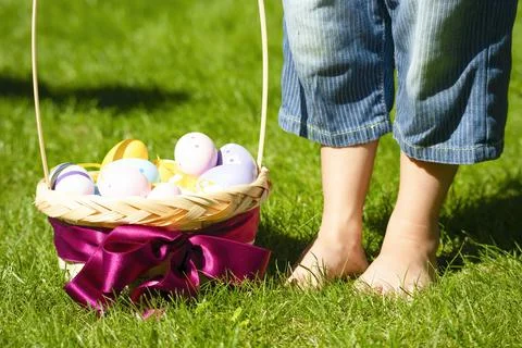 Basket with colorful Easter eggs on a green lawn, children's bare feet Stock Photos
