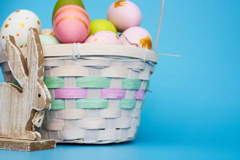 A basket of Easter eggs with toy bunny on blue background.  Festive basket wi Stock Photos