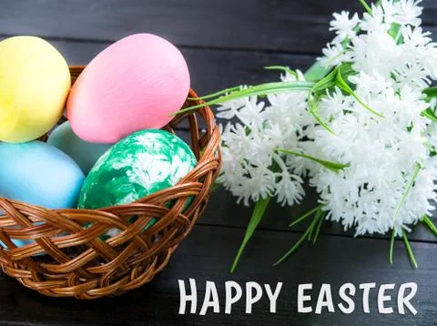 Basket with Easter eggs, white flowers on a dark wooden background Stock Photos