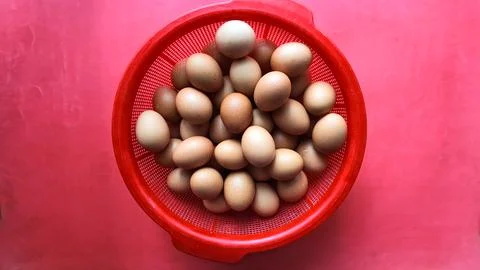 A basket overflowing with brown eggs set against a vibrant red background Stock Photos